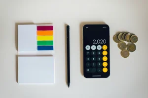Calculadora, notas adhesivas, pluma y monedas de euros sobre mesa blanca