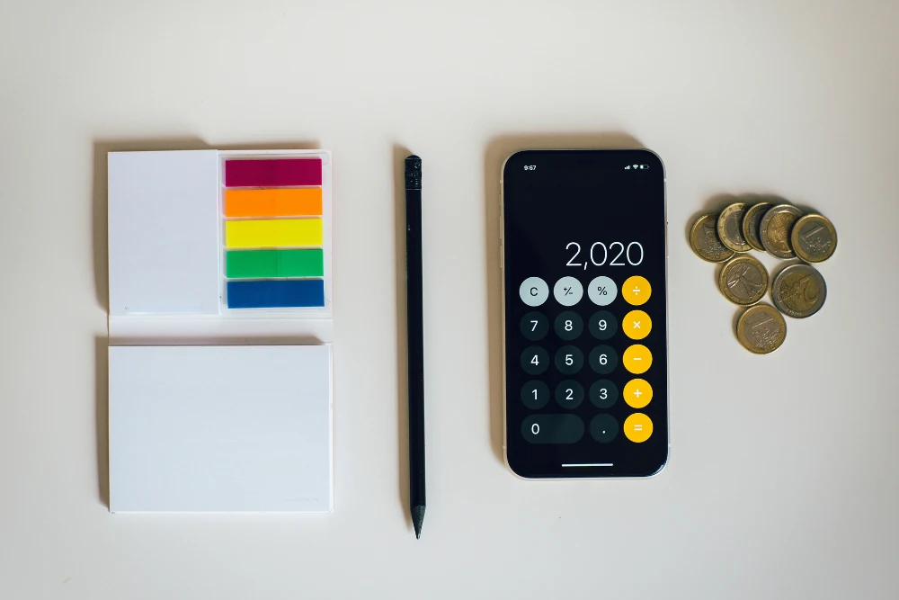 Calculadora, notas adhesivas, pluma y monedas de euros sobre mesa blanca