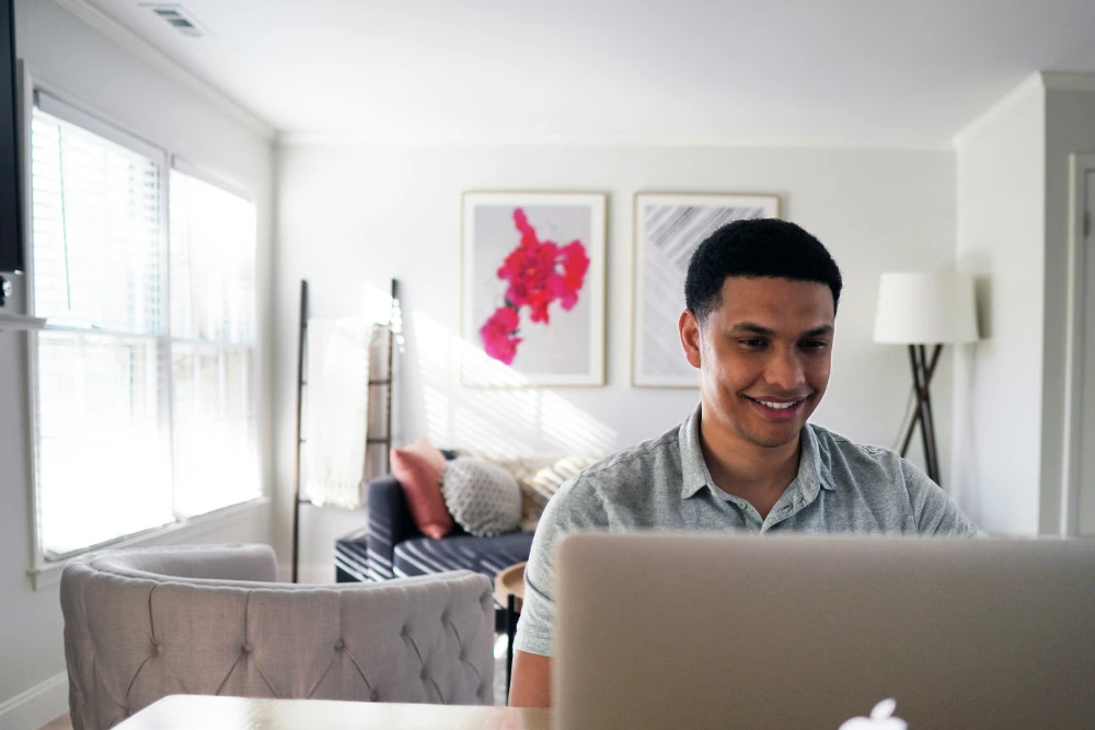 Broker trabajando desde su computador en la sala de su departamento sonriendo