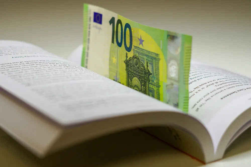 Libro abierto con un billete de 100 euros en entre las páginas de la guia definitiva de Libertad Financiera con Bienes Raices