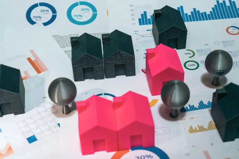 Hojas con gráficos con números al fondo con figuras de casas de monopolio al frente rojas y negras