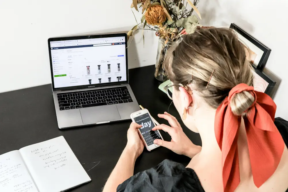 Mujer sentada frente a su compuadora con su telefono inteligente gestionando citas con clientes