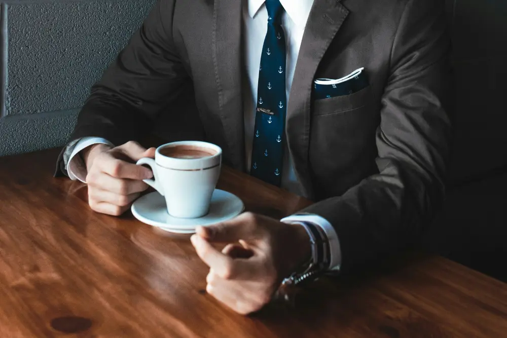 Inversionista elegante con traje tomando un café mientras considera opciones de FInanciamiento inmobiliario inteligente