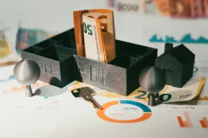 Tablero con figura de casa impresa en 3d con un villere de 50 eurosy una llave sobre grafficos de tasas de interés inmobiliarias en chile