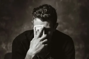 Hombre sentado mirando a la cara con un fajo de billetes de 100 dolares cubriendo su cara haciendo alución a impuestos en la inversión inmobiliaria